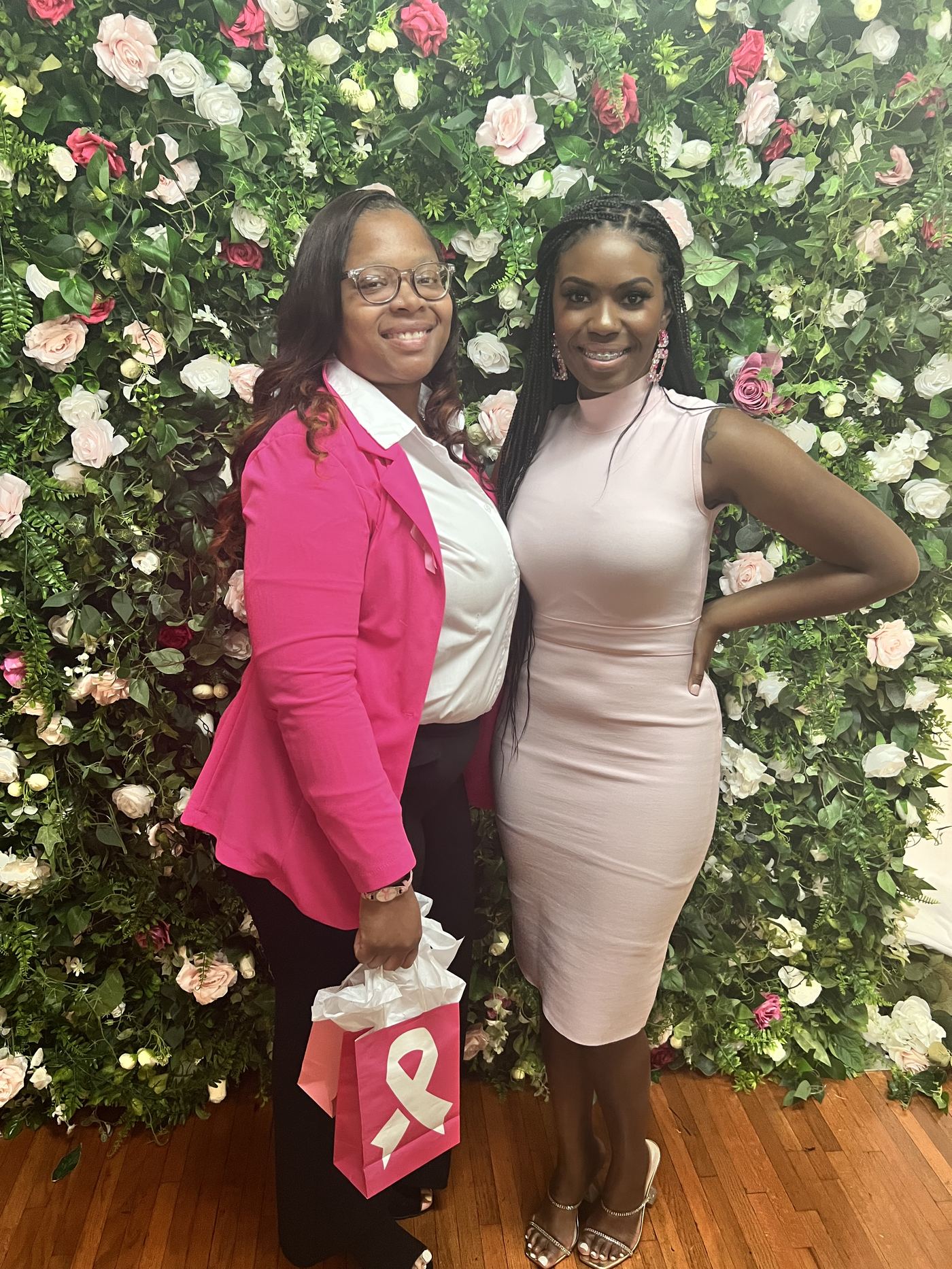 Two guests posing at the floral wall with a gift bag